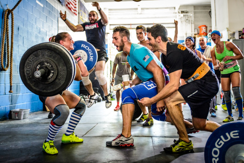 What the hell are you doing CrossFit?
Why are you getting all up in this chicks grill IN THE MIDDLE OF A LIFT?
I hope she fails the lift and dumps the weight forward.
Blue Shorts will try to get out of the way but the bar will hit him right in the knee wraps he doesn’t need.
The collision of the olympic bar with Blue Shorts’ shin causes him to spill his Venti Non-Fat One Pump No-Whip Mocha Latte all over the floor.
Blue Shorts starts bleeding everywhere, so Black Shirt takes off his belt (he wasn’t using it anyway) to use as some sort of CrossFit tourniquet.
The guy jumping in the background sees the stupidity of the situation and comes over to tell Black Shirt that he is functionally retarded.
Jumping Man slips on the puddle of coffee and ends up headbutting Black Shirt.
Finally an ambulance arrives to take away all the CrossFitters gains.
End of story.